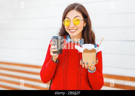 Nahaufnahme der jungen asiatischen Frau mit Kaffeetasse und Wok Nudeln Papierbox auf der Straße der Stadt Stockfoto