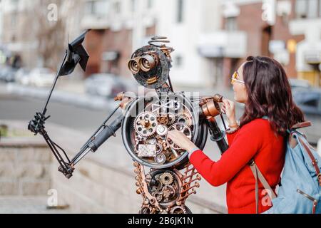 28. APRIL 2018, UFA, RUSSLAND: Frau berührt Roboterstatue, die aus Müll und Metallabfällen auf der Straße der Stadt Ufa entstanden ist Stockfoto