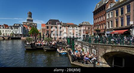 Stadt Leiden, Provinzland Südholland, Niederlande, am Kanal Galcewater, mit terrassenförmigen Booten entlang der Hoogstraat donker Straße, die flachen Boote vermoorten sich in eine Höhle? Restaurant die Menschen, die Sonne genießen, die Stadt Leiden ist bekannt für ihre säkulare Architektur, seine Kanäle, seine Universitof 1590, die nativitof Rembrand, die Stadt, in der die erste Tulpe Europas im 16. Jahrhundert geblüht wurde Stockfoto