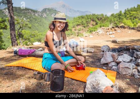 Eine Frau organisiert ein Camp-Leben auf einem Zeltplatz, der auf einer Matte in den Bergen sitzt Stockfoto