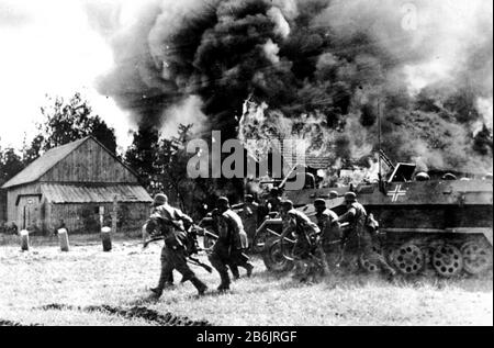 OSTVORDERE deutsche Soldaten ziehen im Jahr 1941 durch ein brennendes russisches Dorf, unterstützt von einem gepanzerten Personalträger Stockfoto