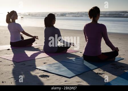 Rückansicht der Frauen, die am Strand Yoga machen Stockfoto
