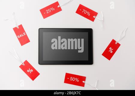 Online-Shopping-, Verkaufs- und Marketingkonzept - Tablet-pc-Computer und rote Tags mit Rabattzeichen auf weißem Hintergrund Stockfoto