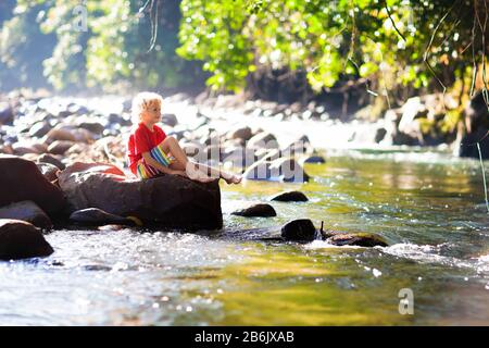 Kinder, die in den Alpen wandern, überqueren den Fluss. Kinder spielen auf dem Berg in Österreich im Wasser. Familienurlaub im Frühling. Kleiner Junge auf Wanderpfad. Im Freien Stockfoto