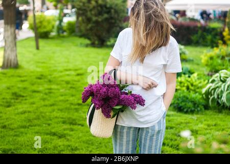 Frau, die einen lebhaften Haufen lilakischer Blumen im Frühlingspark hält, grünes Gras, Lebensstil, Mädchen mit Blumen Stockfoto