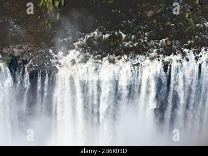 Luftaufnahme eines beeindruckenden Volumens von Wasser, das in den Victoria Falls, Simbabwe in Afrika fließt. Hohe Sicht auf Wasserfälle. Sprühnebel und Sprühnebel aus Wasser. Stockfoto