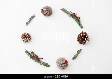 Winterurlaub, Neujahr und Dekorationskonzept - Rahmen aus Tannenzweigen mit roten Beeren und Kiefernkegeln auf weißem Grund Stockfoto
