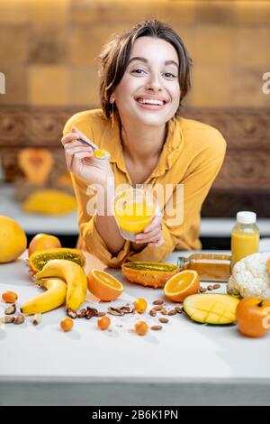 Portrait einer jungen und fröhlichen Frau, die chia Pudding isst, einen Snack oder ein Frühstück in der Küche mit viel frischem Obst und Gemüse hat. Konzept von Vegetarismus, gesundem Essen und Wellness Stockfoto