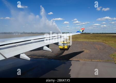 Luftfahrt-Wasserkanone salutieren nach Ankunft am Flughafen Victoria Falls (VFA/FVFA) an Bord des Airbus A340 von South African Airways. Blick auf den Flügel von innen. Stockfoto