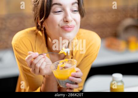 Portrait einer jungen und fröhlichen Frau, die chia Pudding isst, einen Snack oder ein Frühstück in der Küche hat. Konzept der Ernährung, gesunden Ernährung und Wellness Stockfoto