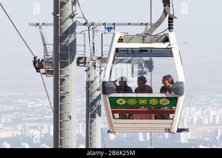 Luftseilbahn in Ashgabat, Turkmenistan mit drei einheimischen Turkmeninnen, die traditionelles grünes Nationalkleid und Schal an Bord des Wagens tragen. Stockfoto