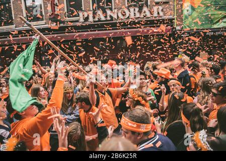 Orangefarbene Partygänger übernehmen die Straßen Amsterdams, um den Geburtstag von König Willem-Alexander am Koningsdag zu feiern. Stockfoto