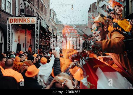 Orangefarbene Partygänger übernehmen die Straßen von Amsterdam, um den Geburtstag des Königs am Koningsdag zu feiern. Stockfoto