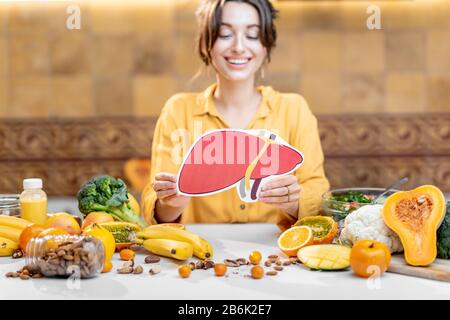 Frau, die das Modell der menschlichen Leber mit einer Vielzahl von gesunden frischen Lebensmitteln auf dem Tisch hält. Konzept einer ausgewogenen Ernährung für die Gesundheit der Leber Stockfoto