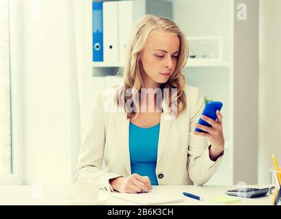 Geschäfts-, Technologie-, Menschen- und Kommunikationskonzept - Geschäftsfrau textet im Büro auf Smartphone Stockfoto