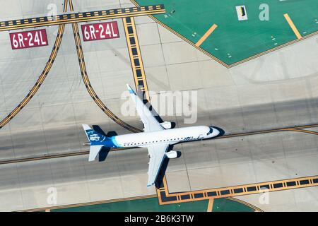 Luftbild der Alaska Airlines Embraer 175, die von Horizon Air auf dem LAX/KLAX-Flughafen betrieben wird. Rollbahn- und Landebahnmarkierungen für Verkehrsmuster auf dem Asphalt. Stockfoto