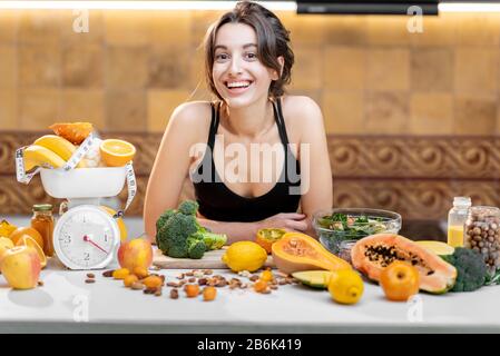 Portrait einer Sportlerin in Sportswear mit viel gesundem frischen Essen in der Küche. Konzept des Gewichtsverlustes, des Sports und des gesunden Essens Stockfoto