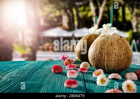 Frische Kokosnussgetränke und verschwommene exotische Bäume und Restauranthintergrund im Freien. Schöner sonniger Hintergrund im Sommer. Platz für Werbeprofi kopieren Stockfoto