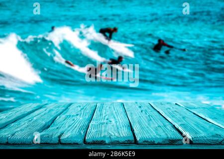 Surfer auf Wellen im türkisfarbenen Ozean. Blauer Holztisch mit Platz für Ihre Dekoration und Werbemittel. Fröhliche aktive sonnige Sommerzeit Stockfoto