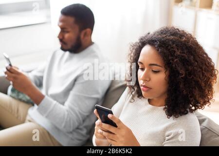 Technologie-, Internet- und Personkonzept - afro-amerikanisches Paar mit Smartphone zu Hause Stockfoto