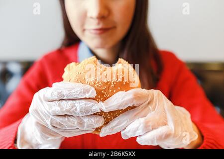 Frauenhände in Handschuhen, die Burger im modernen Fastfood-Restaurant halten Stockfoto