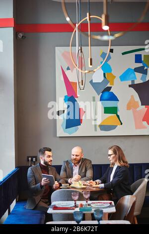 Der junge Manager, der Tablet verwendet, präsentiert seinen Kollegen kreative Projekte bei Meetings im angesagten Café Stockfoto