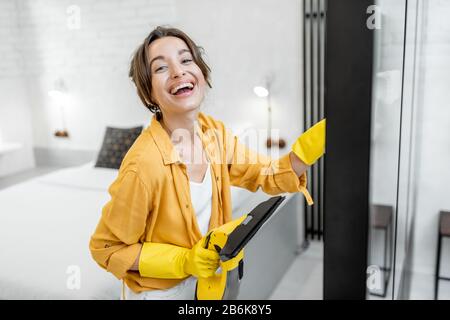 Portrait einer glücklichen Frau, die Glaswände mit einem speziellen Reinigungsgerät zu Hause waschen soll. Konzept einer professionellen Ordnung und Sauberkeit Stockfoto