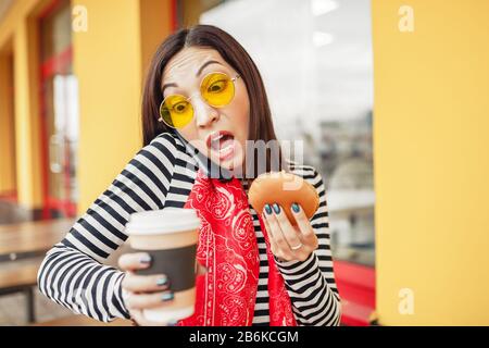 Überraschte beschäftigte Frau, die während eines Abendessens in einem Fast-Food-Restaurant telefoniert Stockfoto