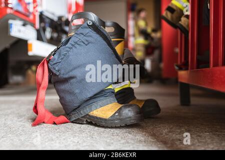 Feuerwehrschuhe und -Hosen und ein schrank, Feuerwehrwagen und Feuerwehrmann im Hintergrund Stockfoto