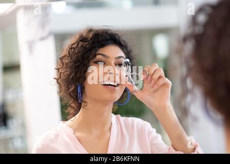 Brünette lächelnde Frau, die ihre Wimpern mit einem Lockenstab kräuselt Stockfoto