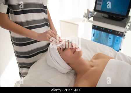 Kosmetologe im gestreiften Hemd, das Kunden im Gesicht säubert Stockfoto