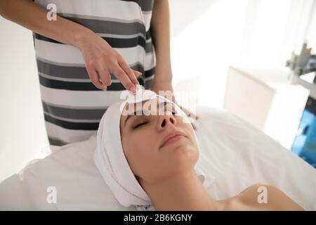 Kosmetologe im gestreiften Hemd, das Kunden mit Baumwollschwamm reinigen Stockfoto