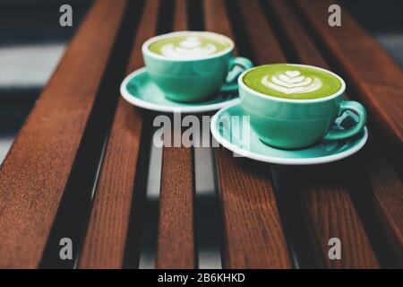 Zwei Tassen Cappuccino und Latte Kunst auf Holz- Hintergrund. Schönen Schaum, grün Keramik Tassen, stilvolle, Tonisierung, Platz für Text. Stockfoto