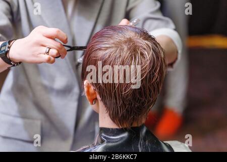 Schließen Sie die Hände des Friseursalons, indem Sie die Haare des Kunden mit einer Schere junger Frau im Schönheitssalon schneiden Stockfoto