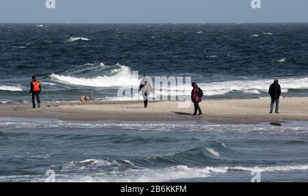 Wustrow, Deutschland. März 2020. Spaziergänger sind auf der Halbinsel Fischland an der turbulenten Ostsee. Sonne und Squalls bis zu Force Eight sorgen für eine beeindruckende Kulisse. Credit: Bernd Wüstneck / dpa-Zentralbild / dpa / Alamy Live News Stockfoto