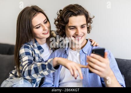 Süßes Paar auf Couch mit Smartphone zu Hause im Wohnzimmer entspannen Stockfoto