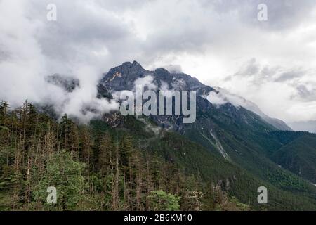 Der Schnee-Berg Jade Dragon, Yulong Xueshan, durchbricht Wolken und Nebel in Lijiang, Provinz Yunnan, China. Die Gletscher sind das ganze Jahr über zu sehen. Stockfoto