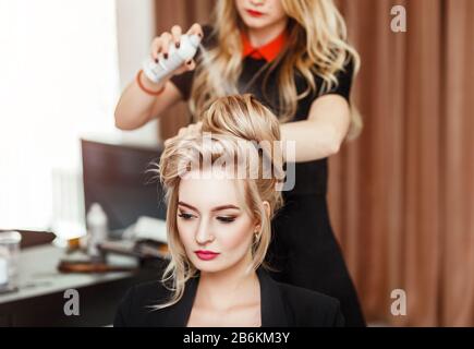 Professioneller Friseur mit Haarspray auf die Haare der Geschäftsfrau des Kunden im Schönheitssalon Stockfoto