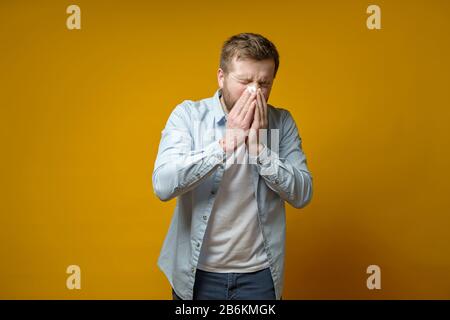 Der Mann ist krank, hat eine laufende Nase, er hustet oder niest und bedeckt den Mund mit einem Taschentuch. Konzept der Verbreitung des Virus. Stockfoto