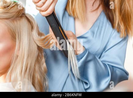 Glätten und kräuseln blonder Haare im Friseursalon mit Bügeleisen Stockfoto