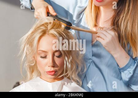 Glätten und kräuseln blonder Haare im Friseursalon mit Bügeleisen Stockfoto