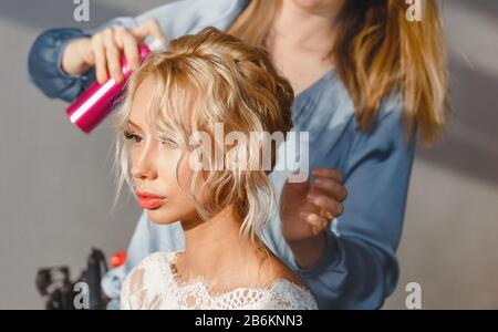 Ein Coiffeur im Friseursalon macht eine Frisur und fixiert sie mit einem Spray Stockfoto