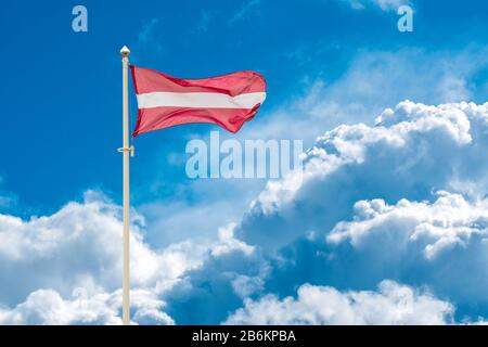 Lettische Nationalflaggen winken auf Wind gegen blau bewölkten Himmel Stockfoto