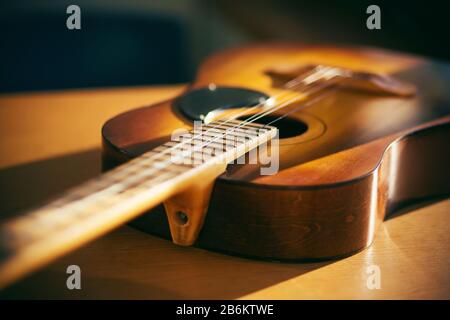 Auf einem Holztisch liegt eine alte Akustikgitarre, der Saiten fehlen und von hellem Sonnenlicht beleuchtet wird. Stockfoto