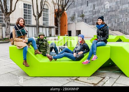 Eine Gruppe von Freunden, die Spaß haben und auf der Bank im Park in Wien sitzen Stockfoto