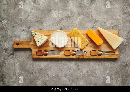 Sortiment von verschiedenen Arten von Käse auf Holzbrett mit Messer und Gabel serviert. Stockfoto