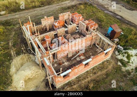 Luftbild der Baustelle für zukünftiges Ziegelhaus, Betonfundament und Stapel gelber Lehmziegel für den Bau. Stockfoto