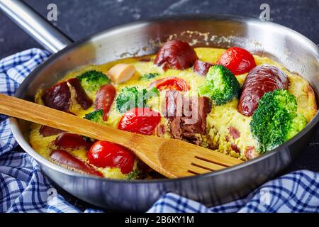 Heiße italienische Frittata mit Würstchen, Brokkoli, Kirschtomaten, geschmolzenem Käse in einem Skillet auf einem Betontisch Stockfoto