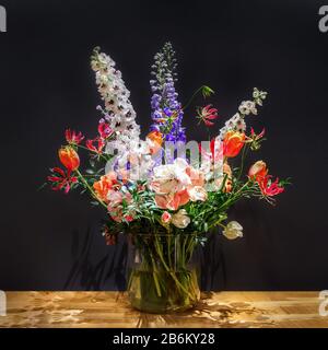 Luxuriöser Blumenstrauß aus gemischten Blumen in Glasvase auf Holztischoberfläche Vor dunkelgrauem Hintergrund. Stillleben oder Hochzeitsdekor. Stockfoto
