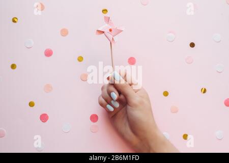 Kinderpastellwetter-Topf für einen Cupcake in der Hand eines Mädchens mit Maniküre auf pinkfarbenem Hintergrund mit Konfetti. Geburtstag festliche Hintergründe. Stockfoto
